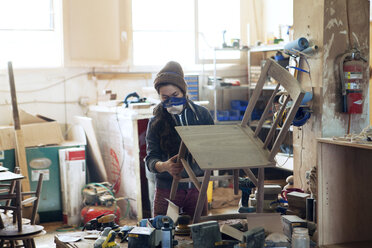 Female carpenter examining wooden chair in workshop - CAVF07438