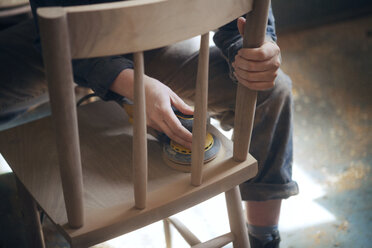 Midsection of female carpenter sanding wooden chair at workshop - CAVF07458