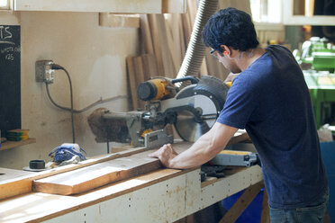 Seitenansicht eines männlichen Zimmermanns, der ein Holzbrett mit einer elektrischen Säge schneidet - CAVF07464