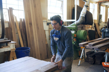 Male carpenter holding wooden plank at workshop - CAVF07481