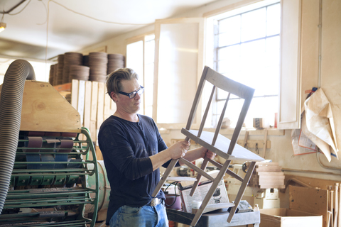 Männlicher Tischler, der einen Holzstuhl in einer Werkstatt untersucht, lizenzfreies Stockfoto
