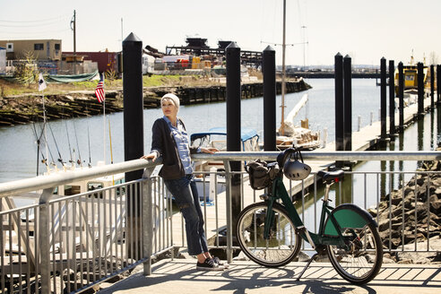 Frau lehnt sich mit dem Fahrrad am Hafen an ein Geländer - CAVF07517