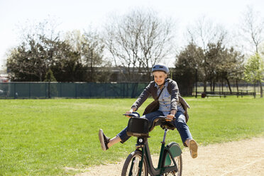 Fröhliche Frau spielt beim Fahrradfahren im Park - CAVF07519