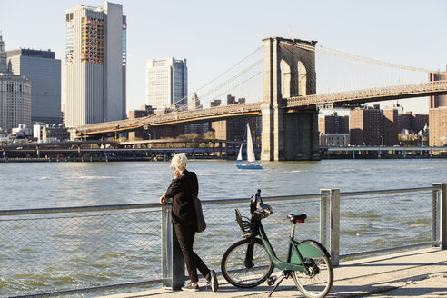 Frau schaut auf die Brooklyn Bridge über den East River, während sie auf der Promenade steht - CAVF07523