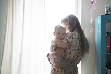 Mutter trägt Baby am Fenster stehend - CAVF07536