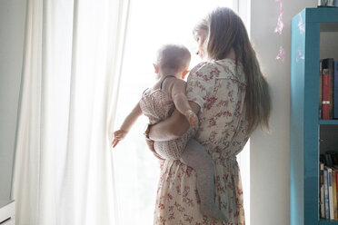 Mutter trägt Baby am Fenster zu Hause - CAVF07537