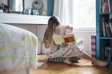 Mutter liest mit ihrem Baby ein Buch, während sie zu Hause auf dem Boden sitzt - CAVF07539