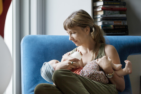 Mother feeding milk to baby with bottle at home stock photo