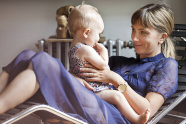 Mutter spielt mit Baby, während sie zu Hause auf einem Sessel sitzt - CAVF07560