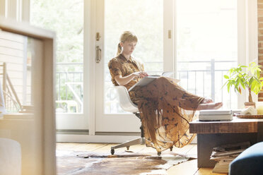 Woman reading book while sitting on chair at home - CAVF07570