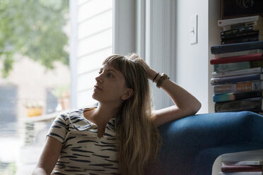 Nachdenkliche Frau, die zu Hause auf dem Sofa vor dem Fenster sitzt - CAVF07573