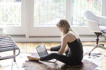 Woman using laptop while sitting on floor at home - CAVF07578