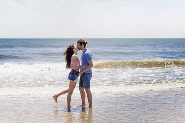 Affectionate couple kissing while standing on shore at beach stock