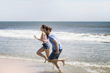 Side view of couple running on shore at beach during summer vacation - CAVF07599