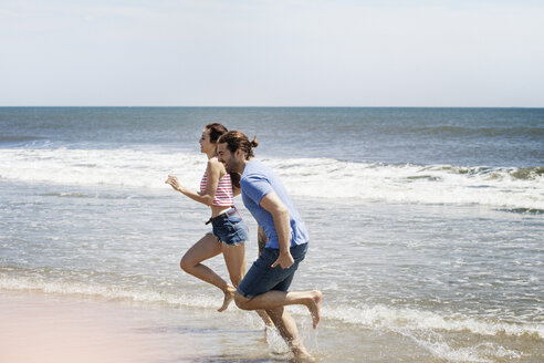 Seitenansicht eines Paares, das in den Sommerferien am Strand läuft - CAVF07599