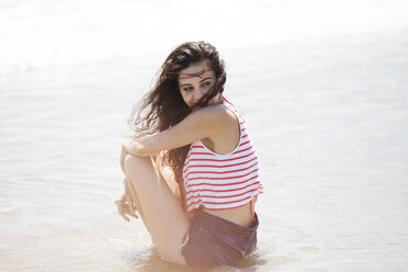 Seitenansicht einer nachdenklichen Frau, die am Ufer eines Strandes sitzt - CAVF07601
