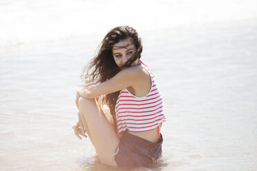 Side view of thoughtful woman sitting on shore at beach - CAVF07601