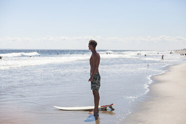 Man looking away while standing at shore with surfboard - CAVF07615