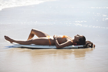 Frau entspannt sich auf einem Surfbrett am Ufer - CAVF07619