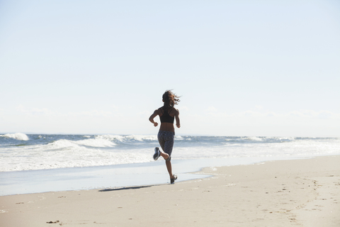 Rückansicht einer am Strand laufenden Frau an einem sonnigen Tag, lizenzfreies Stockfoto
