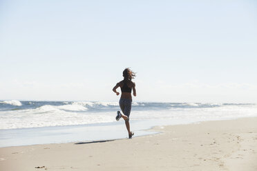 Rear view of woman running at beach on sunny day - CAVF07624