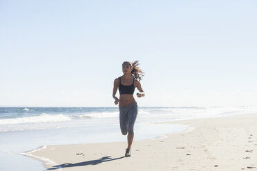 Confident woman jogging on shore at beach against sky - CAVF07625