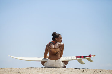 Rear view of woman with surfboard sitting at beach - CAVF07636