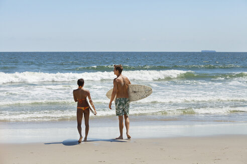Rückansicht eines Paares mit Surfbrett am Strand - CAVF07643