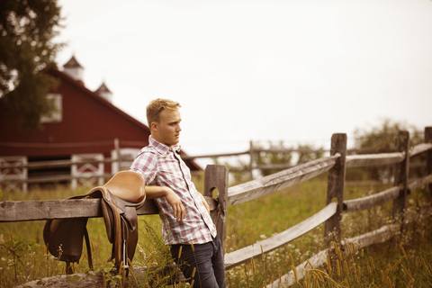 Rancher lehnt sich an einen Zaun und steht auf einem grasbewachsenen Feld, lizenzfreies Stockfoto
