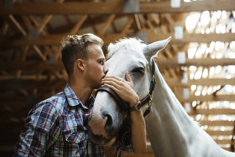 Niedriger Winkel Blick auf Rancher küssen Pferd im Stall, lizenzfreies Stockfoto