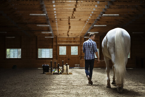 Rückansicht eines Ranchers, der mit einem Pferd im Stall spazieren geht - CAVF07670