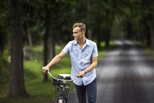 Mann schaut weg, während er mit dem Fahrrad auf einer Straße im Wald geht - CAVF07674