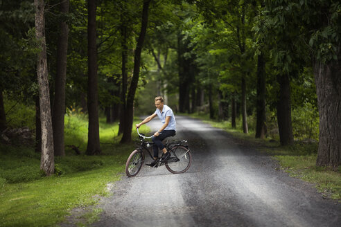 Glücklicher Mann fährt Fahrrad auf einer Straße im Wald - CAVF07676