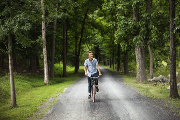 Glücklicher Mann beim Radfahren auf der Straße im Wald - CAVF07678