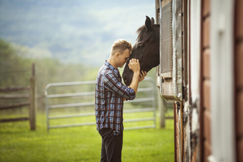 Rancher streichelt Pferd, das durch den Stall auf dem Bauernhof späht - CAVF07679