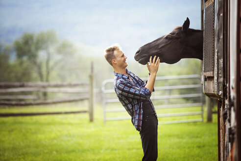 Glücklicher Rancher schaut auf ein Pferd, das durch den Stall späht - CAVF07681