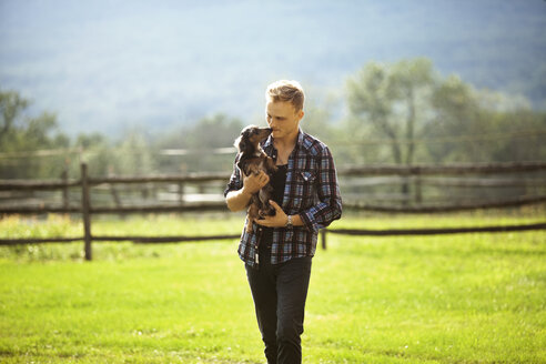 Mann mit Hund beim Spaziergang auf einem grasbewachsenen Feld auf einem Bauernhof - CAVF07682