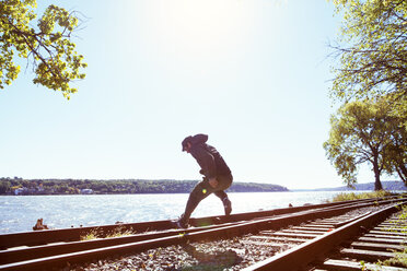 Mann springt auf Eisenbahnschienen am Fluss gegen klaren Himmel - CAVF07740