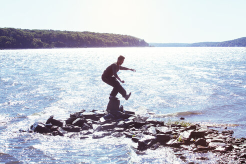 Side view of man balancing on rock in river against clear sky - CAVF07741