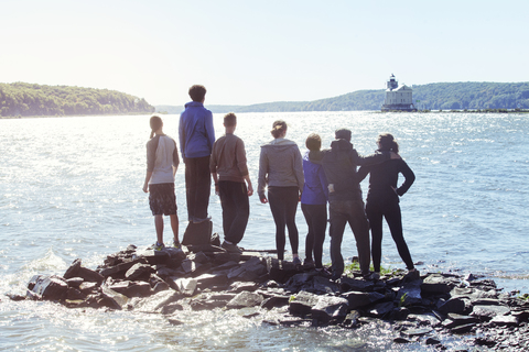 Rückansicht von Freunden, die auf Felsen im Fluss stehen, gegen den klaren Himmel, lizenzfreies Stockfoto