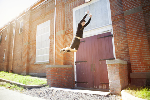 Mann springt an sonnigem Tag durch eine Ziegelmauer, lizenzfreies Stockfoto