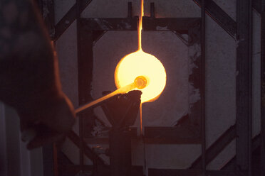 Ausgeschnittenes Bild eines Glasbläsers, der eine Glasmacherpfeife im Ofen einer Glasfabrik erhitzt - CAVF07764