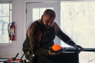 Handwerker hält eine Glasmacherpfeife mit geschmolzenem Glas in der Werkstatt - CAVF07771