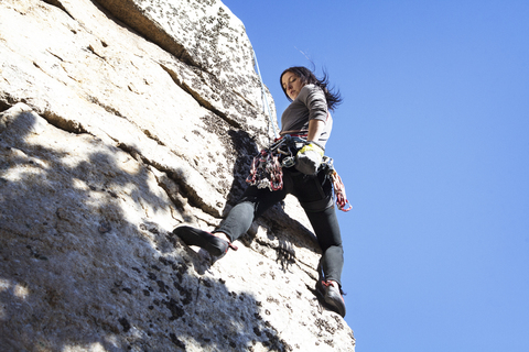 Low angle view of woman rock climbing against clear blue sky stock photo