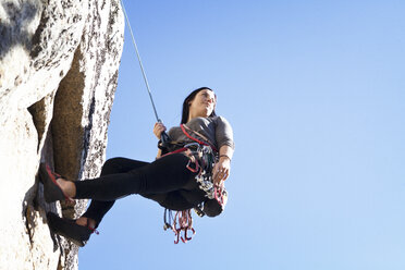 Low angle view of woman rappelling against clear blue sky - CAVF07821