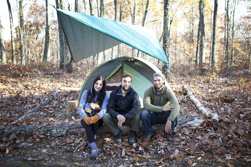 Porträt von Freunden, die auf einem umgestürzten Baumstamm neben einem Zelt im Wald sitzen - CAVF07832