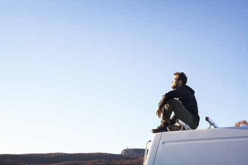 Seitenansicht eines auf einem Wohnmobil sitzenden Mannes gegen den klaren Himmel - CAVF07835
