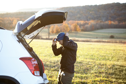 Seitenansicht eines Mannes mit Scheinwerfer, der neben einem Auto auf einem Feld steht, lizenzfreies Stockfoto