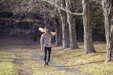 Mann in voller Länge, der Ruder trägt, während er auf einem Feld im Wald geht - CAVF07867