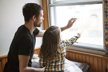 Vater und Sohn malen zu Hause auf dem Bett kniend auf einer Fensterscheibe - CAVF07872